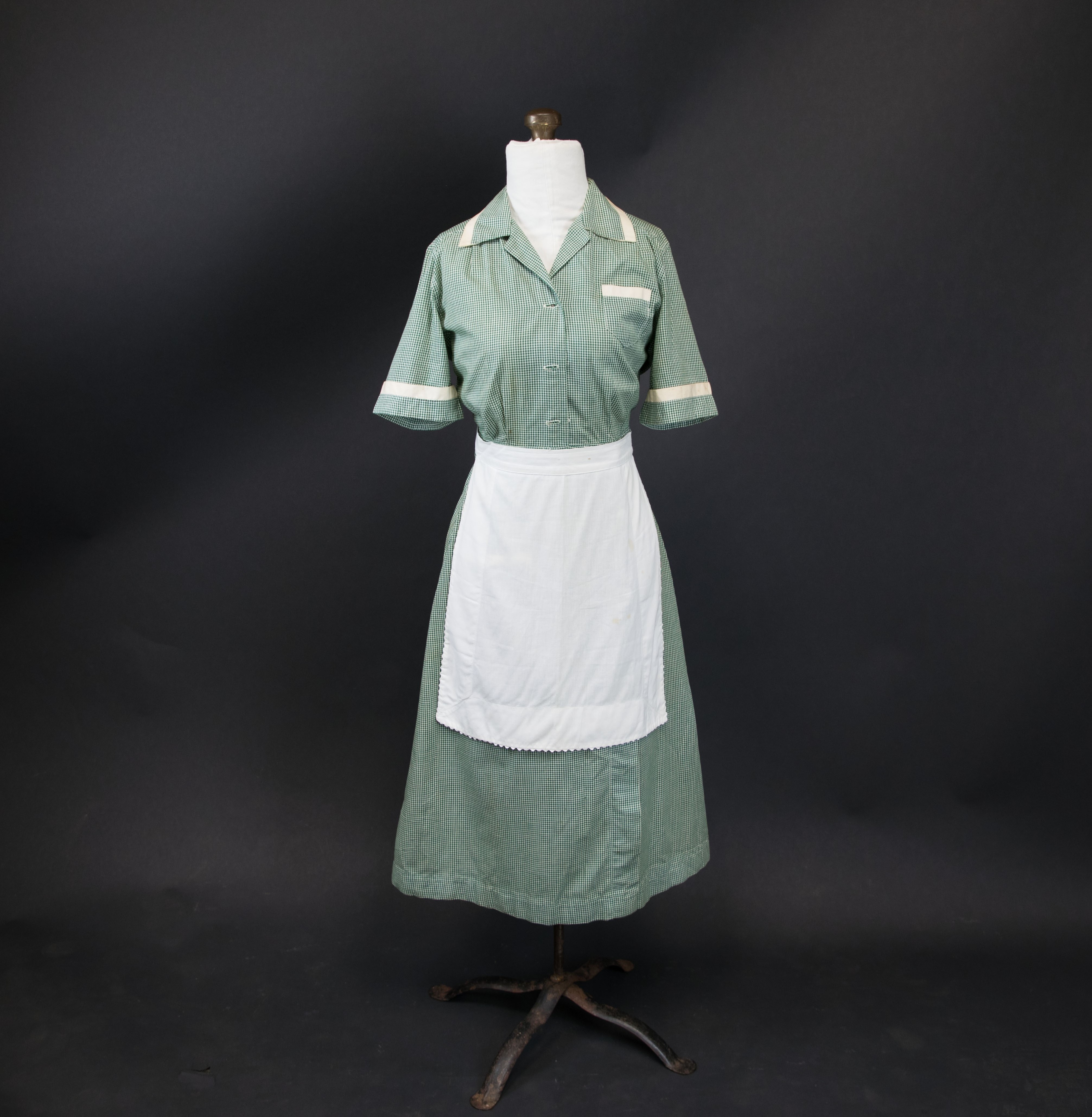 Photograph of a plain grey and white maid's uniform with apron on dress form.